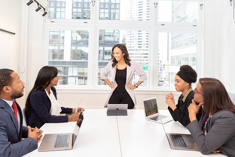 stock photo woman standing at boardroom table with coworkers seated